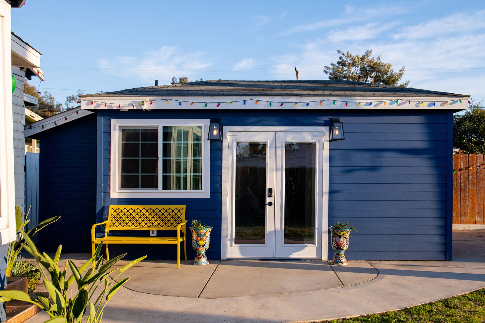 A San Diego garage converted into a navy board-and-batten ADU with French doors and a yellow bench