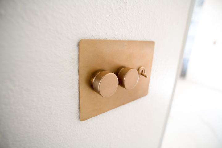 Brass wall plate with two dimmer knobs and a toggle switch on a white wall