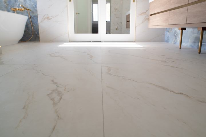 Large-format marble-look floor tiles in a bright bathroom with freestanding tub and floating vanity
