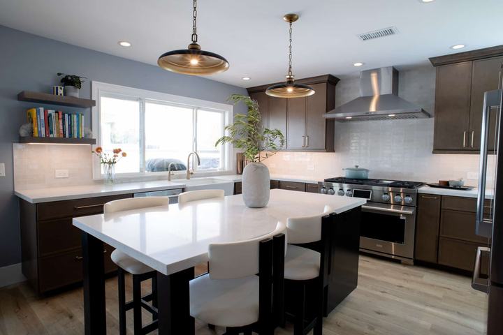 Quartz-topped island on a black base with white upholstered stools under two brass and black pendants