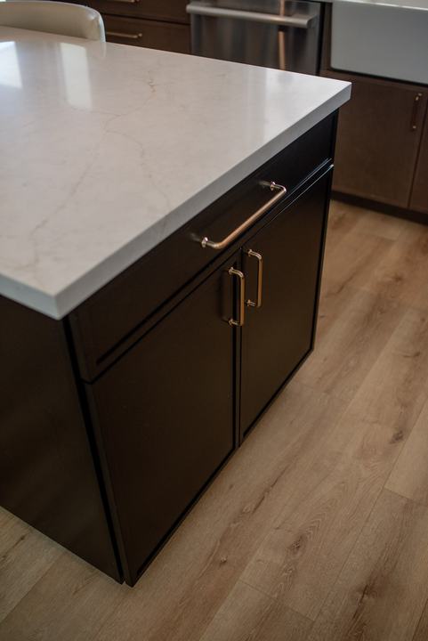 Corner of the black island showing the quartz countertop edge and brass cabinet pulls