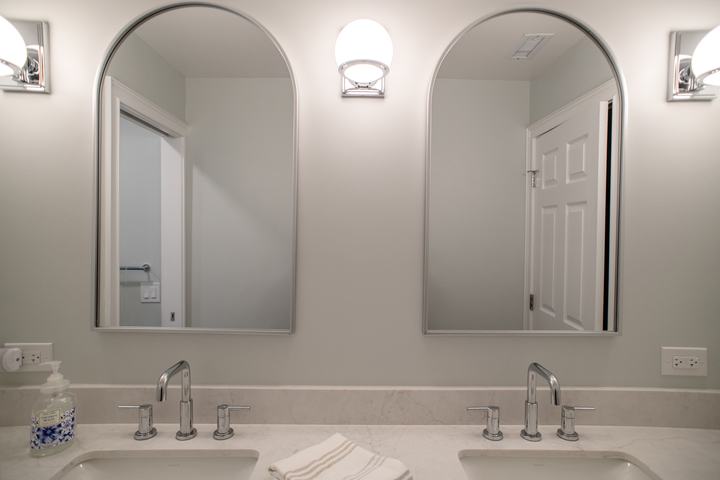 Paired arched mirrors flanking a chrome globe sconce above the counter