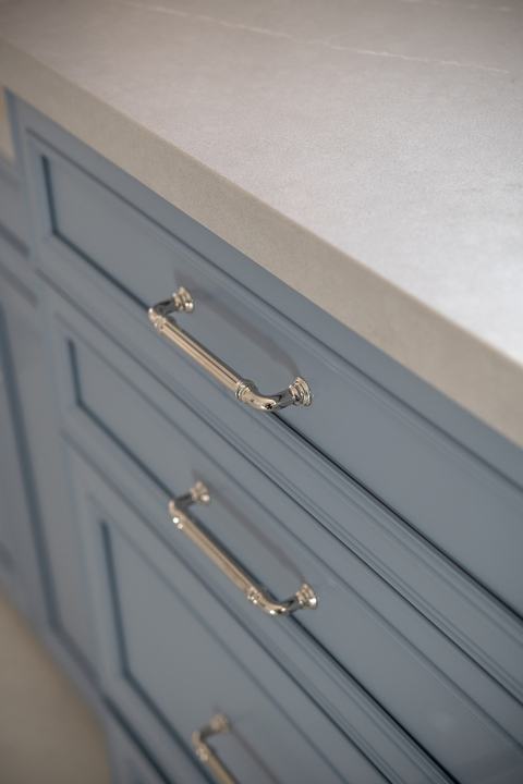 Close-up of quartz countertop edge and polished nickel cabinet pulls on blue vanity drawers