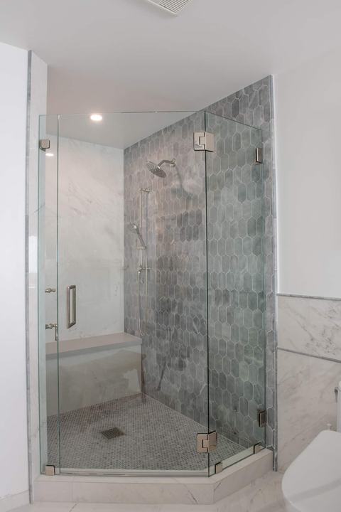 Corner shower with frameless glass panels, blue-gray lotus tile wall, and penny round shower floor