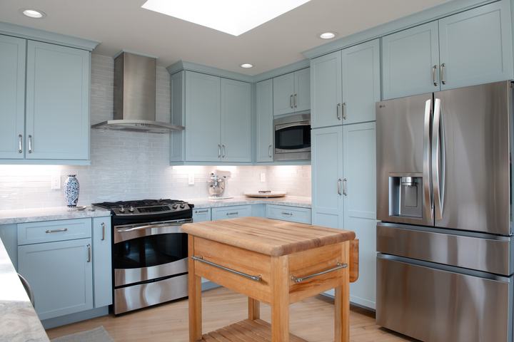 Angled view of remodeled kitchen with blue cabinets, skylight, stainless refrigerator, and butcher-block prep cart