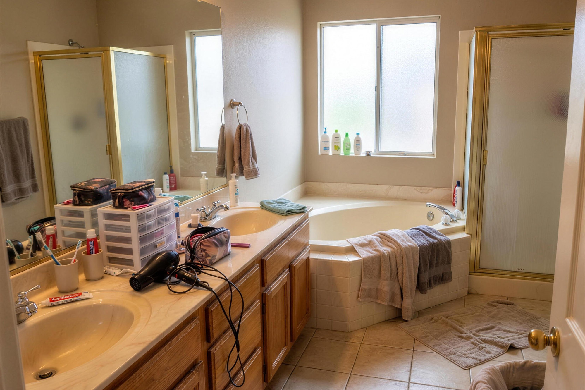 Before: a dated primary bathroom with an oak double vanity, a corner tub and a cluttered counter