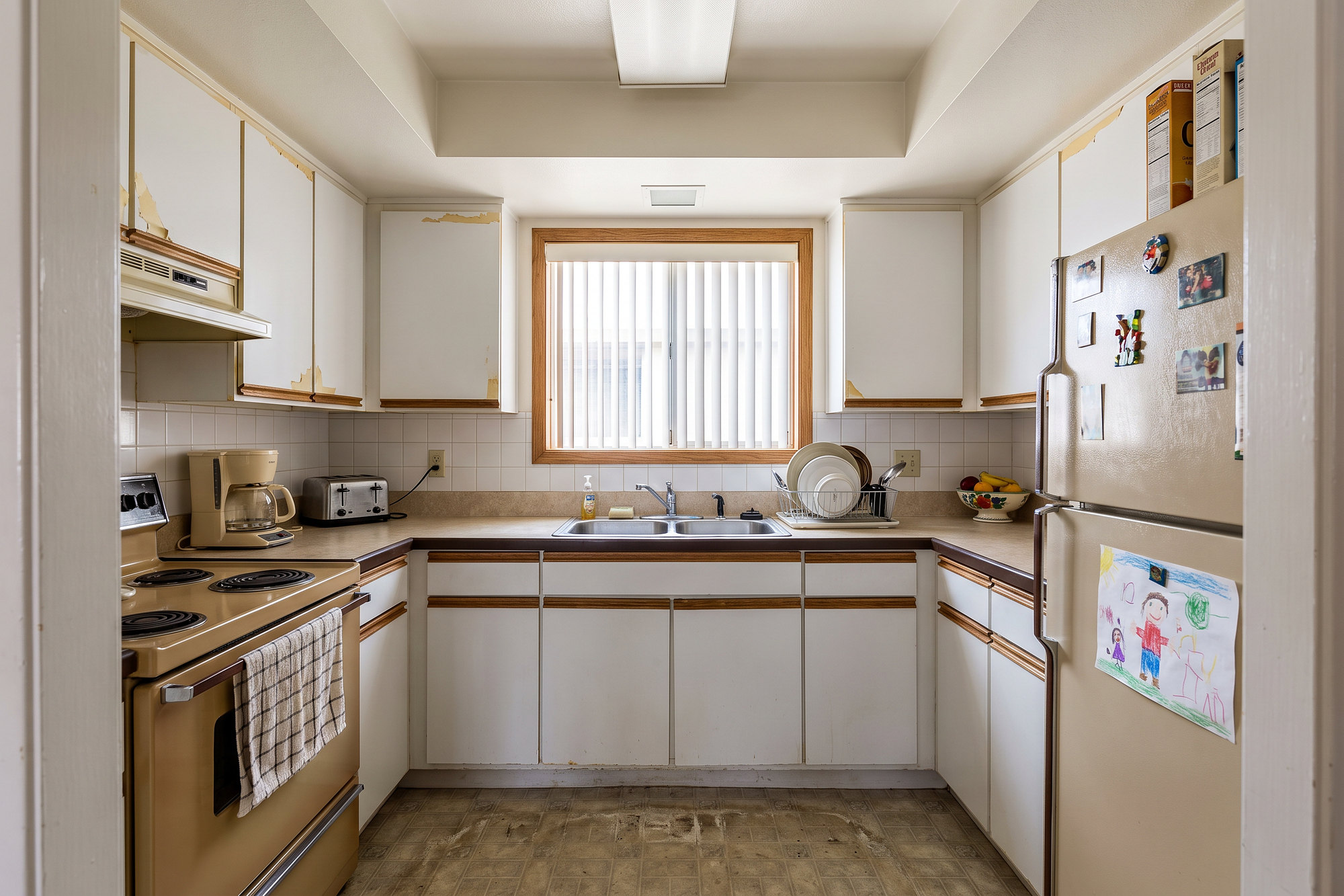 Before: a dated 1990s kitchen with white thermofoil cabinets, beige laminate counters, an almond range and a fluorescent box light