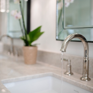 Sink vignette with flowing faucet, quartzite splash ledge and orchid reflected in beveled mirror