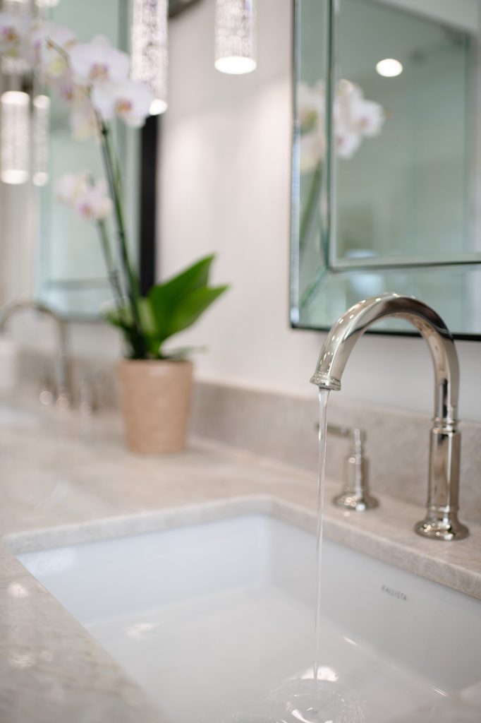 Sink vignette with flowing faucet, quartzite splash ledge and orchid reflected in beveled mirror