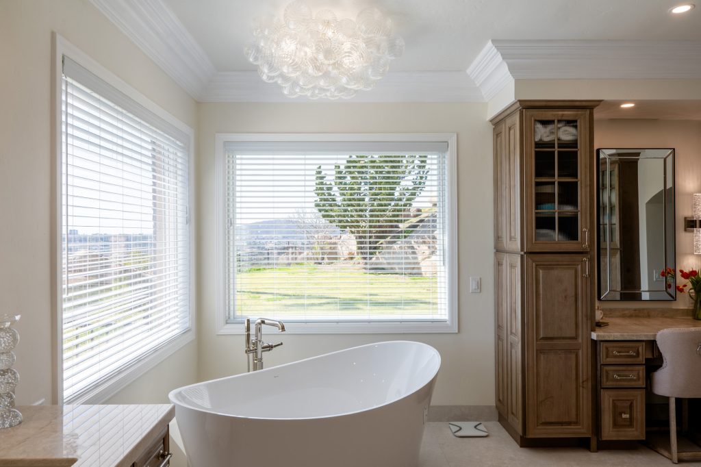 Freestanding micro-bubble tub beneath bubble-glass chandelier, makeup vanity and window view of Poway hills