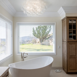 Freestanding micro-bubble tub beneath bubble-glass chandelier, makeup vanity and window view of Poway hills