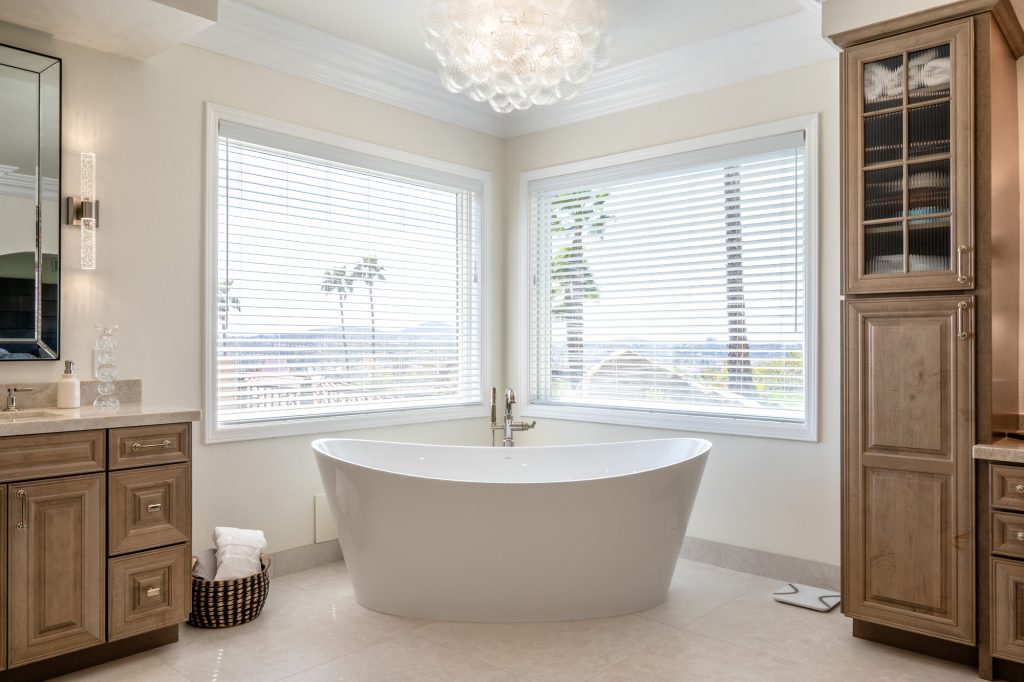 Corner BainUltra tub framed by picture windows with hillside view and bubble chandelier above