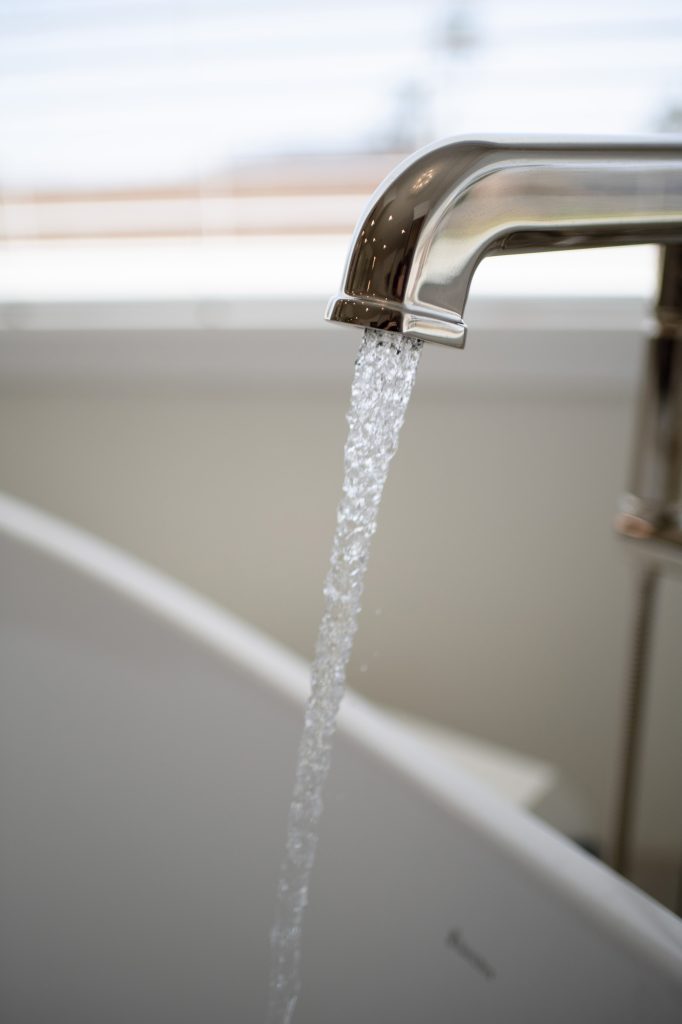 Detail of curved polished-nickel tub spout with streaming water into white freestanding tub