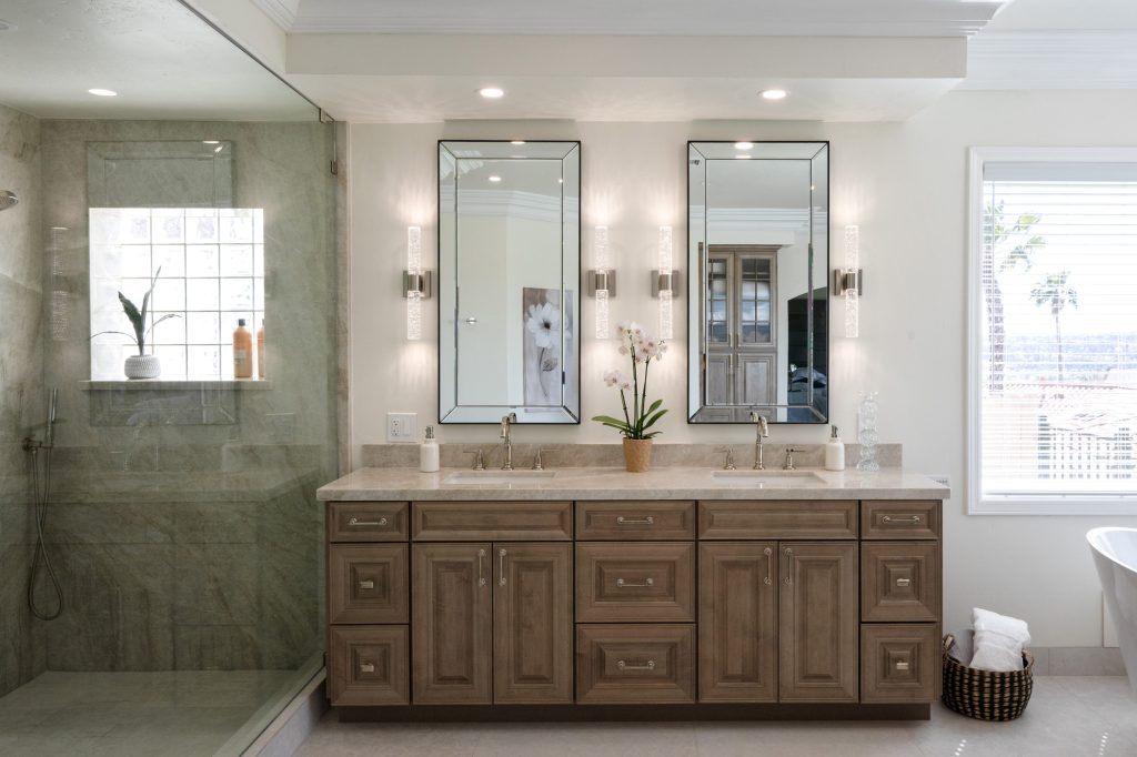 Double-sink vanity with beveled mirrors beside frameless glass shower clad in Taj Mahal quartzite