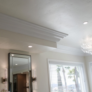 Crown-molded ceiling with glass-bubble chandelier, recessed lights, and palm-framed windows over the vanity area.