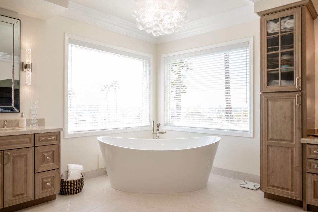 Freestanding oval soaking tub nestled in a windowed corner beneath a glowing glass-bubble chandelier.