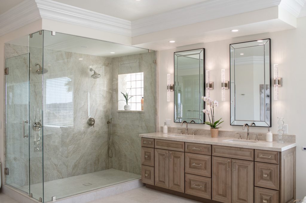 Alternate wide angle of frameless glass shower beside double vanity with beveled mirrors and quartzite tops.