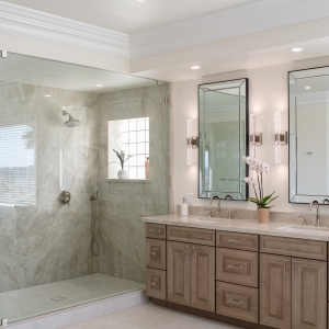 Alternate wide angle of frameless glass shower beside double vanity with beveled mirrors and quartzite tops.