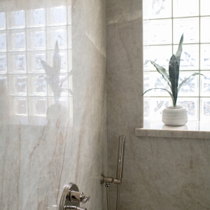 Frameless glass shower wrapped in Taj Mahal quartzite slab walls beside a custom maple-almond double vanity.