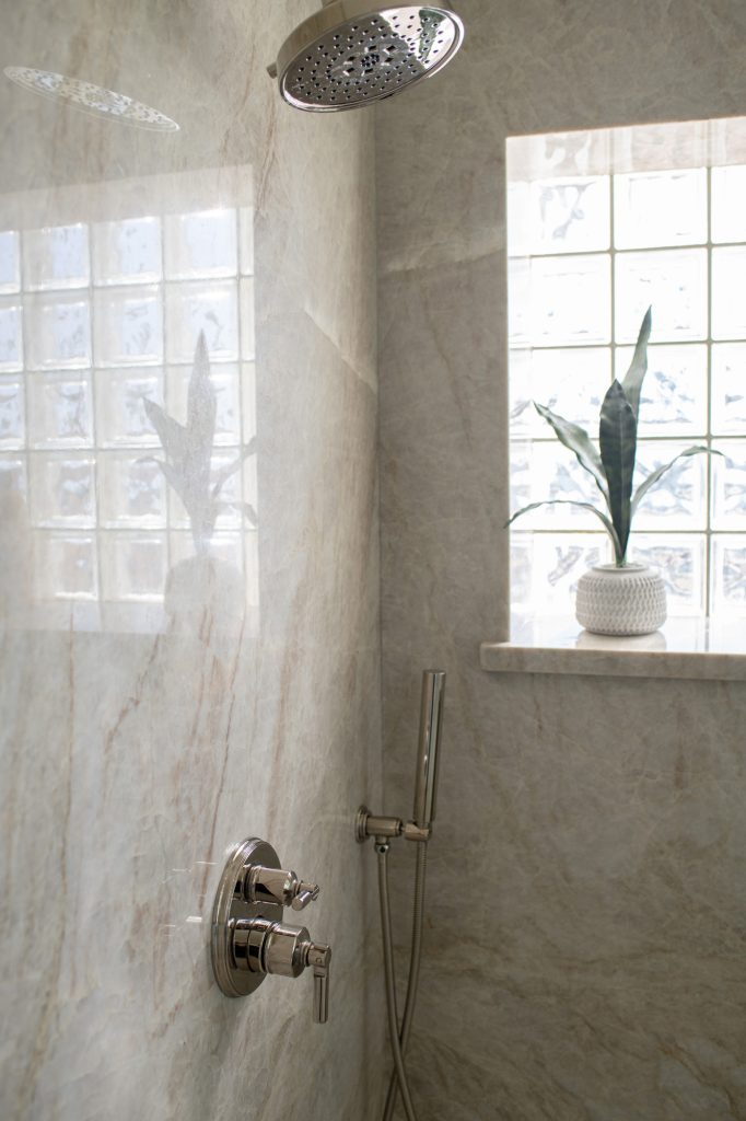 Frameless glass shower wrapped in Taj Mahal quartzite slab walls beside a custom maple-almond double vanity.
