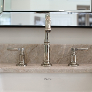 Close-up of polished-nickel Kallista widespread faucet set against a beveled mirror and quartzite backsplash.