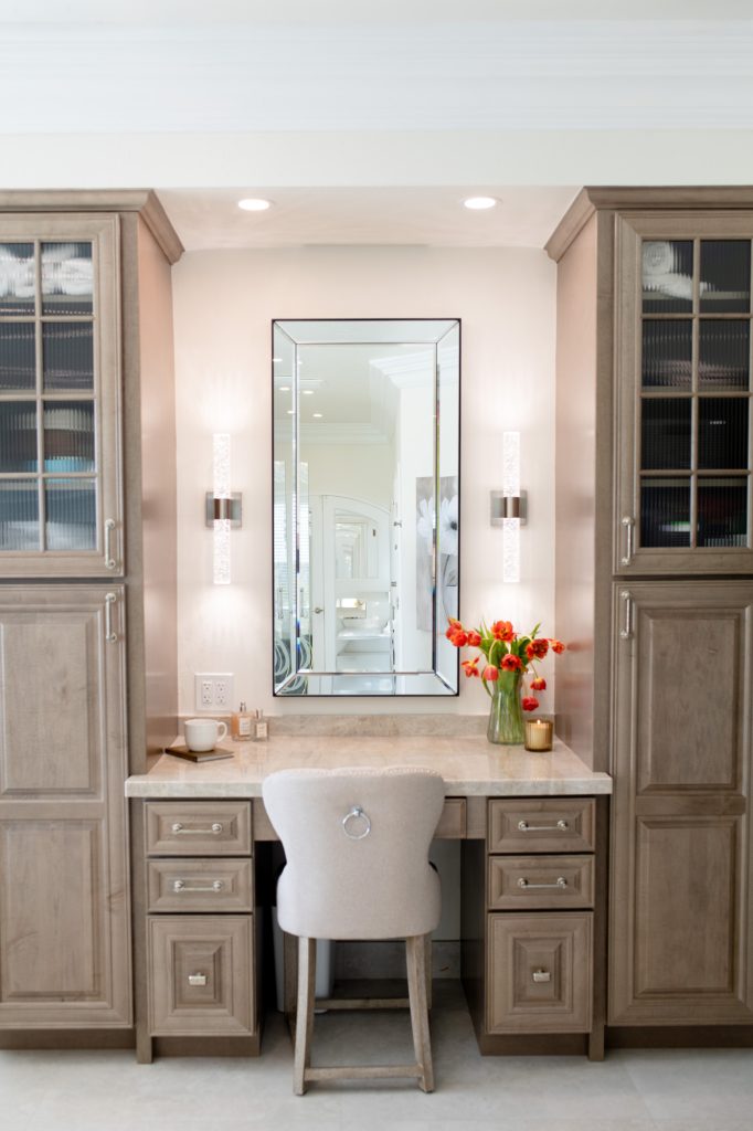 Built-in makeup station flanked by ribbed-glass tower cabinets and an upholstered ring-pull chair.