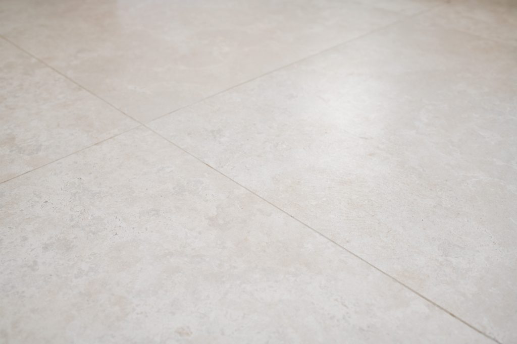 Warm limestone-look porcelain floor tiles in a large-format grid with tight grout joints.
