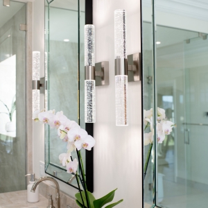 Pair of crystal sconces flanking a beveled mirror above the quartzite vanity with orchid decor.