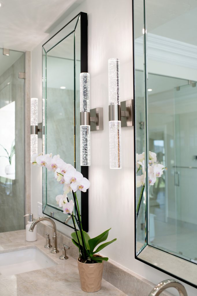 Pair of crystal sconces flanking a beveled mirror above the quartzite vanity with orchid decor.