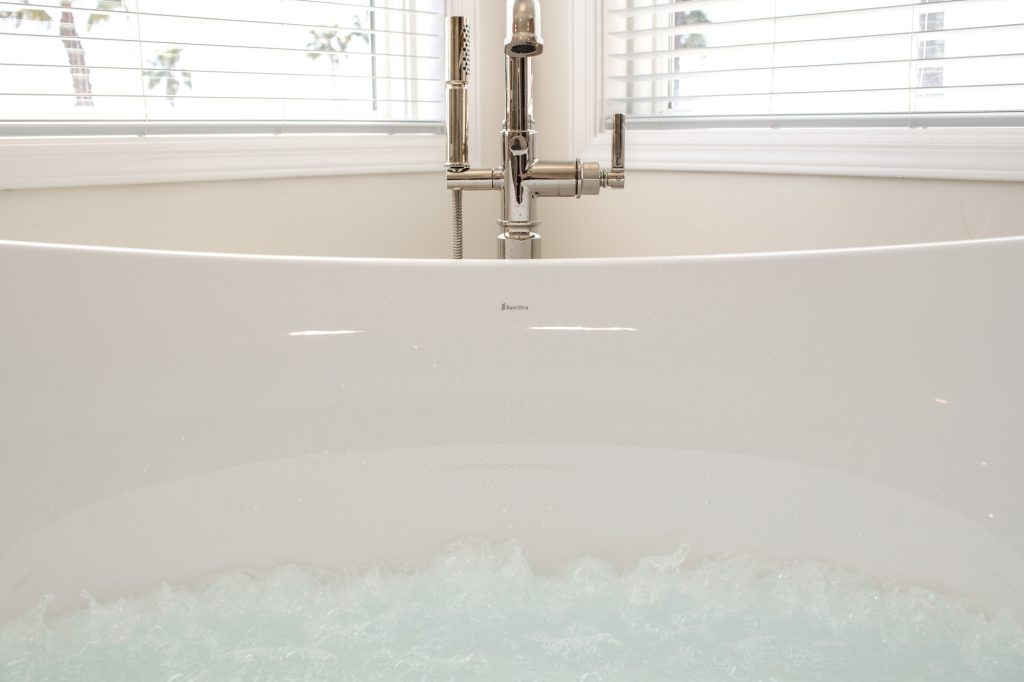 Micro-bubble hydrotherapy churning in the freestanding tub with floor-mount tub filler between corner windows.
