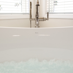 Micro-bubble hydrotherapy churning in the freestanding tub with floor-mount tub filler between corner windows.