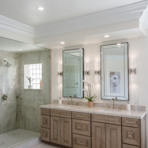 Wide view of double vanity with beveled mirrors and adjacent glass shower in the neutral luxury bath.