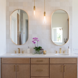 Double-sink maple vanity with brushed-gold faucets and pendant lights.