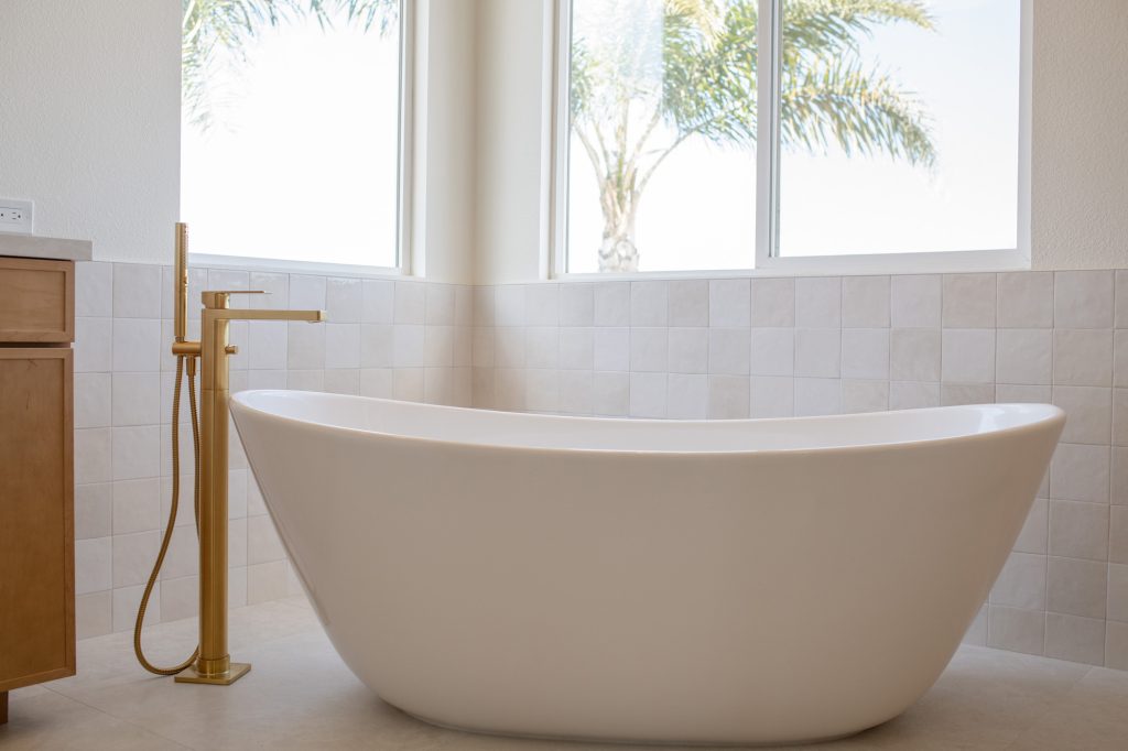 Modern freestanding tub beside floor-mounted brushed-gold filler.