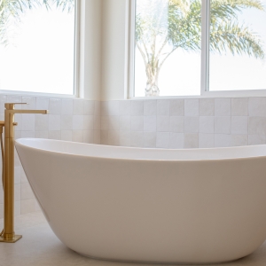 Modern freestanding tub beside floor-mounted brushed-gold filler.
