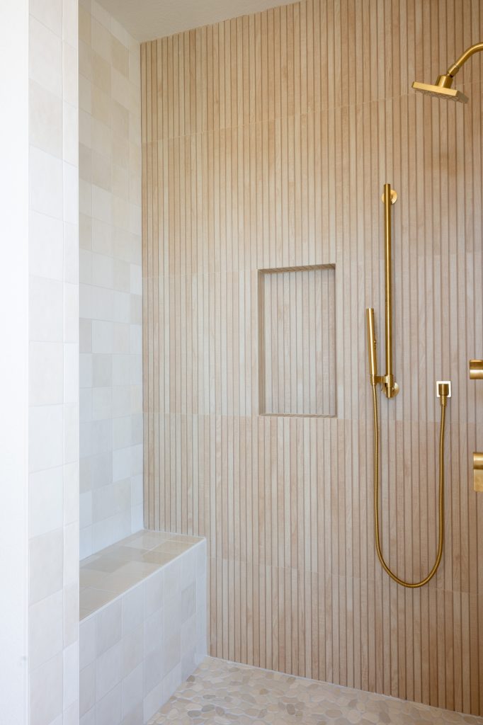 Tiled shower bench and pebble floor meeting vertical slat wall.