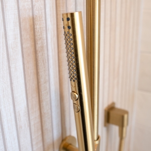 Detail of gold handheld shower wand against slat tile backdrop.