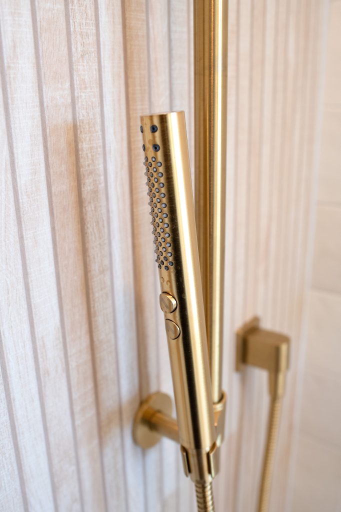 Detail of gold handheld shower wand against slat tile backdrop.