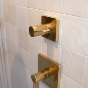 Brushed-gold shower control knobs on glossy neutral tile.