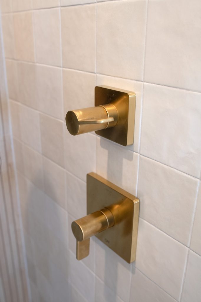Brushed-gold shower control knobs on glossy neutral tile.