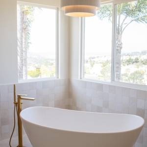 Sculptural tub nestled in windowed corner with tiled wainscot.