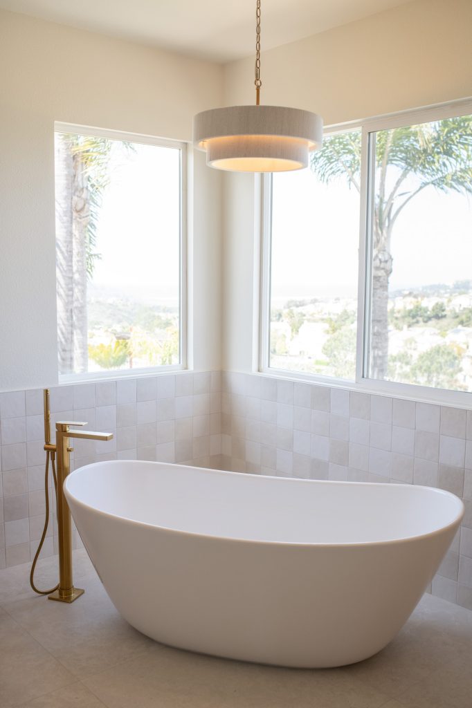 Sculptural tub nestled in windowed corner with tiled wainscot.