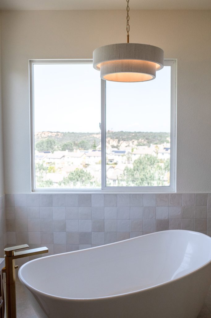 Freestanding tub beneath modern pendant, framed by panoramic window.