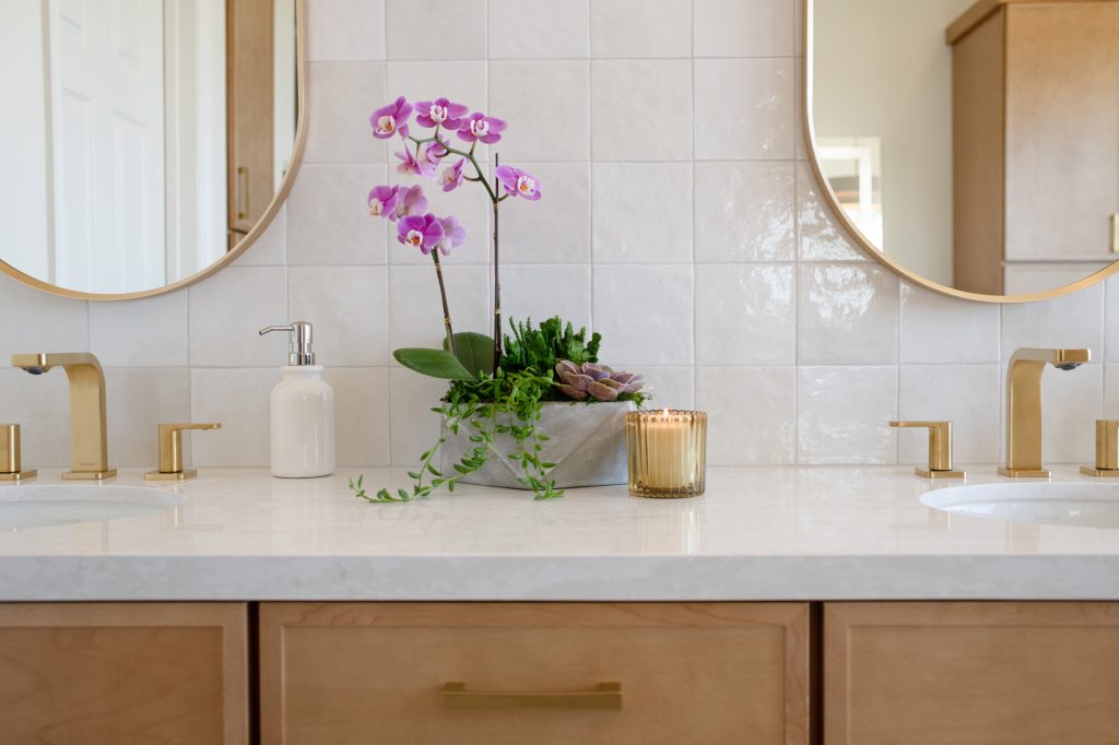 Orchid centerpiece on quartz countertop between twin brushed-gold faucets.