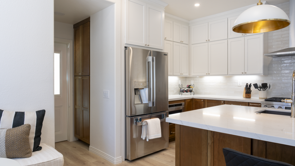 Angle of stainless refrigerator with tall pantry, white uppers, and walnut island countertop in foreground