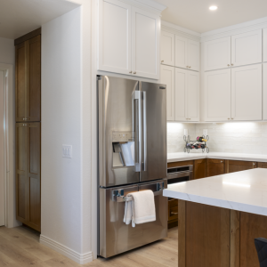 Angle of stainless refrigerator with tall pantry, white uppers, and walnut island countertop in foreground