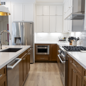 Galley view of remodeled kitchen showing fridge, microwave drawer, range, island sink, and two-tone shaker cabinets