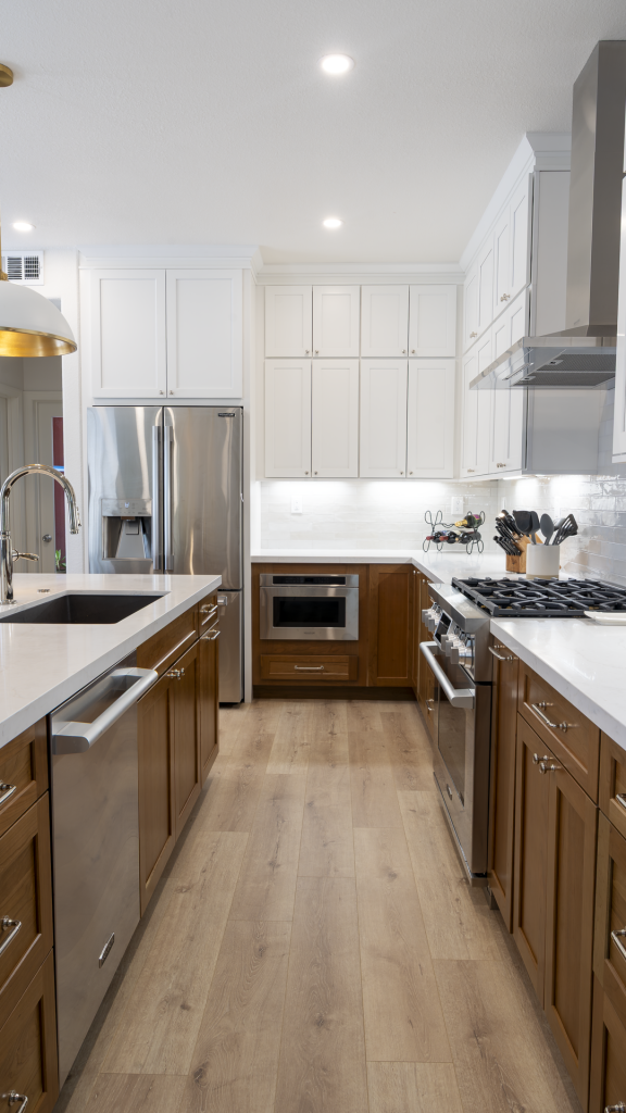 Galley view of remodeled kitchen showing fridge, microwave drawer, range, island sink, and two-tone shaker cabinets