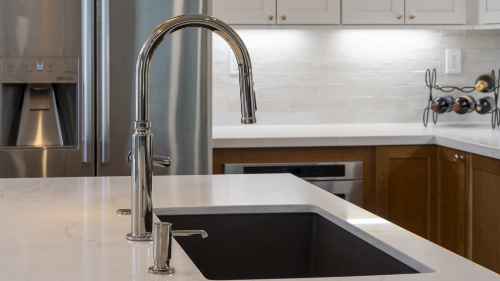 Close-up of chrome pull-down faucet over composite sink set in quartz island; subway backsplash behind