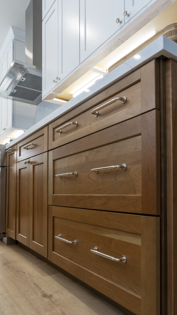 Low-angle detail of walnut drawer fronts with polished-chrome pulls and soft under-cabinet LED lighting